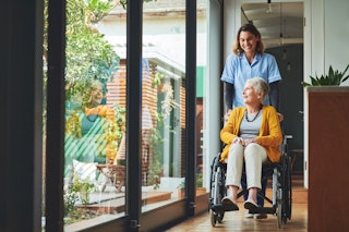 Aînée souriante en fauteuil roulant accompagnée d’une soignante, illustrant l’impact du niveau de soins sur les coûts.
