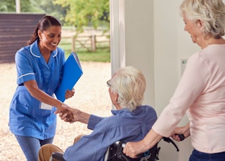 Une infirmière accueillie à domicile par un aîné en fauteuil roulant, illustrant le soutien professionnel essentiel pour vieillir chez soi.