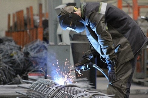 Cette image représente un soudeur penché faisant de la soudure dans une usine.