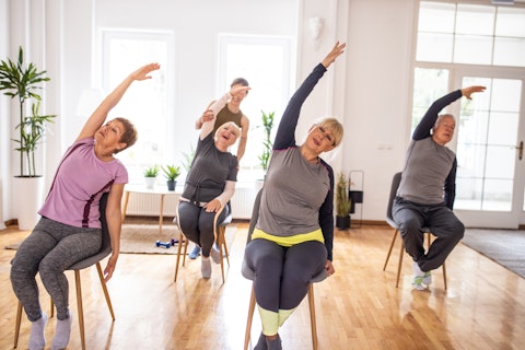 Active senior people practicing yoga during yoga class on chairs in yoga studio